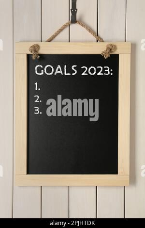 Blackboard with phrase GOALS 2023 and empty checklist on hanging on white wooden background Stock Photo
