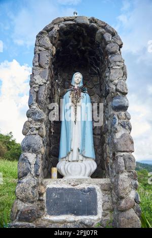 Nov 21, 2023, Puente Nacional, Santander, Colombia: Statue of the Virgin located outdoors with many rosaries hanging and protected in a stone niche. C Stock Photo