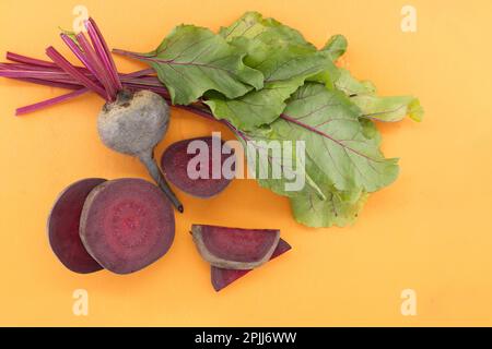 Sliced and whole fresh organic baby beetroot with green leaves on yellow cutting board, top view with free copy space Stock Photo