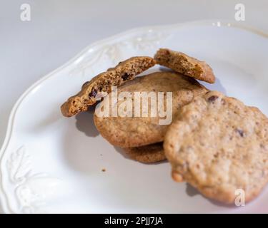 Homemade chocolate chip cookies or biscuits on a white plate with one broken in half. USA. Stock Photo