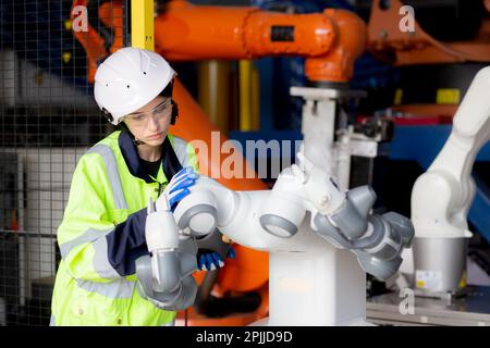 Young engineer woman checking and maintenance machine robot arms technology intelligence and innovation at factory industrial, people or technician ex Stock Photo