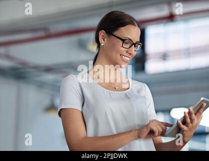 Digitally connected. Young woman using her digital tablet in an industrial office space. Stock Photo