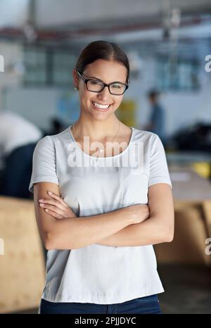 Friendly face of corporate support. Smiling young businesswoman with an open plan office space behind her. Stock Photo