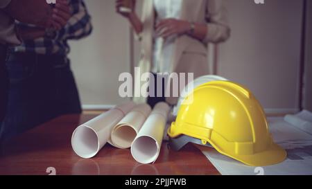Close up view of engineer worktable with safety helmet and blueprint on desk in office room. Stock Photo
