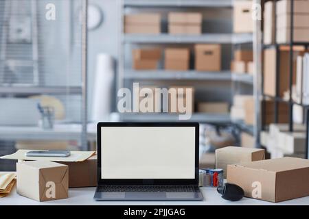 Laptop with blank screen standing among packed boxes containing orders of online clients on workplace of manager of storage room Stock Photo