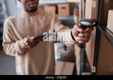Focus on hand of young man holding scanner by one of boxes on shelf while checking codes of packed online orders in storage room Stock Photo