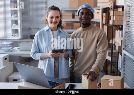 Happy young male and female managers of delivery center or storage room looking at camera with smiles while standing by workplace Stock Photo