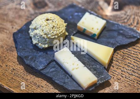 Vegetarian chopping board with tasting of three typical mountain cheeses from northern Italy with Polenta on slate stone plate Stock Photo