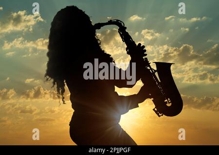 Silhouette of woman playing saxophone against beautiful sky at sunset Stock Photo