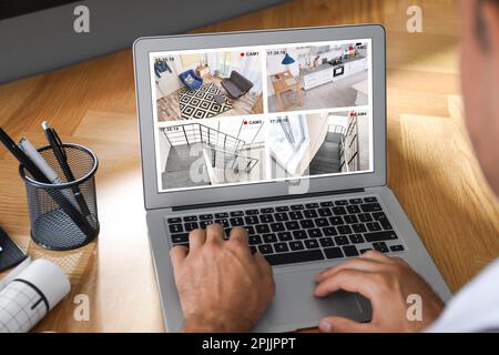Man monitoring modern CCTV cameras at wooden table, closeup. Smart home security system Stock Photo