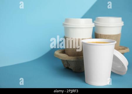 Takeaway paper coffee cups with sleeves, plastic lids and cardboard holder on blue background, space for text Stock Photo
