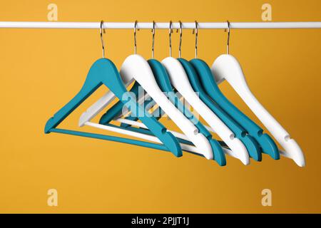 Empty clothes hangers on metal rail against yellow background Stock Photo