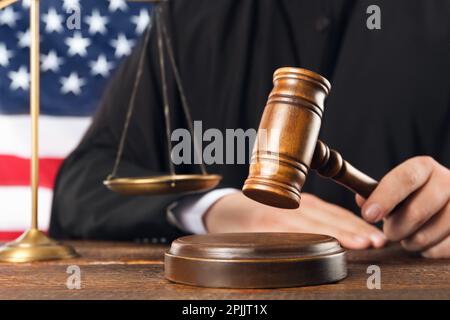 Judge with gavel at wooden table near flag of United States, closeup Stock Photo