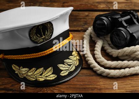 Peaked cap and rope with binoculars on wooden background, closeup Stock Photo