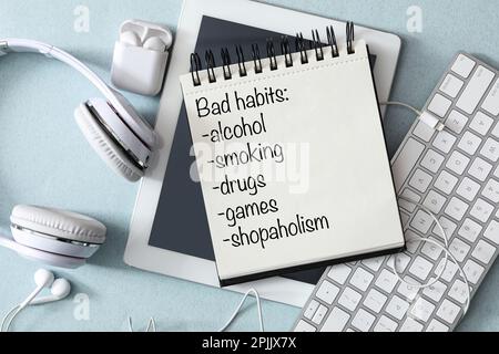 Notebook with list of bad habits, different earphones, tablet and keyboard on light blue table, flat lay Stock Photo