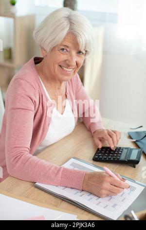 elderly woman sitting at table at home manage budget Stock Photo