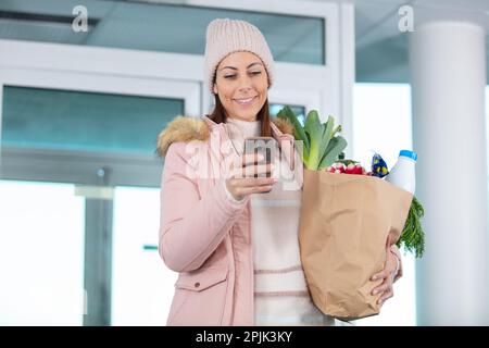young woman using cellphone while coming back from shopping groceries Stock Photo