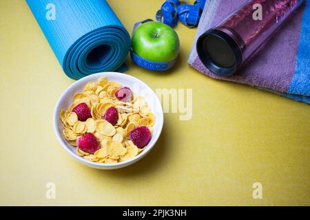 Healthy food, weight loss and diet concept, green apple, measuring tape, gym mat, cereal and bottle of water on a yellow background. Stock Photo