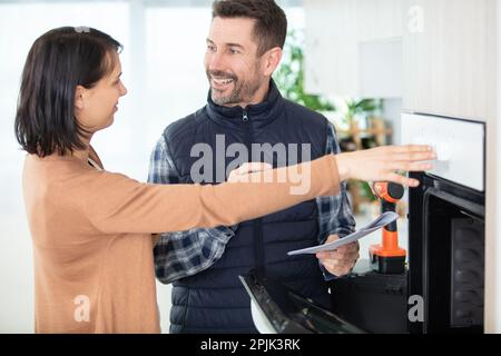 housewife with repairman near modern oven in kitchen Stock Photo
