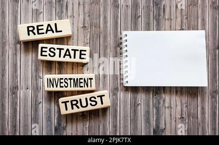 Conceptual words REIT real estate investment fund on wooden blocks on a wooden background next to a notepad for text. Stock Photo