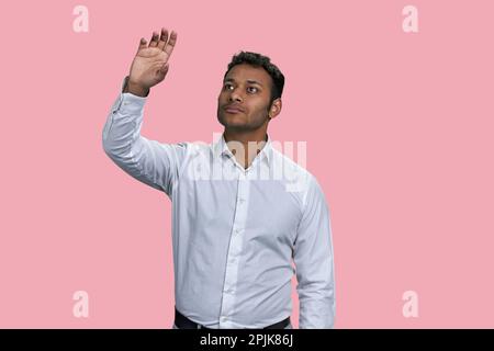 Brown indian businessman touching imaginery virtual screen. Isolated on pink background. Stock Photo