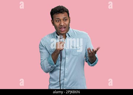 Portrait of a young handsome indian man with microphone. Isolated on pink background. Stock Photo