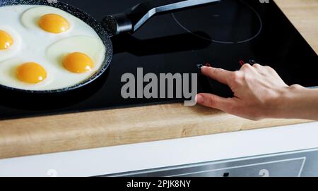 woman cooks breakfast on a frying pan. female cooking  eggs on induction stove. Girl preparing the meal on a modern kitchen Stock Photo