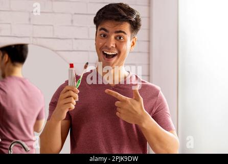 Cheerful young man pointing at toothpaste and toothbrush holding in his hand Stock Photo