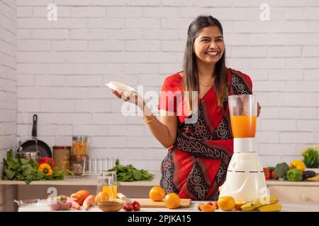 Smiling woman making orange juice in kitchen Stock Photo