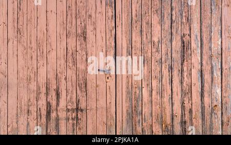 Old double wing wooden garage door with heavily weathered paint Stock Photo