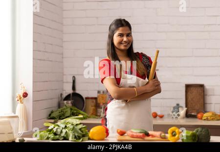 Smiling woman standing with rolling pin in kitchen Stock Photo