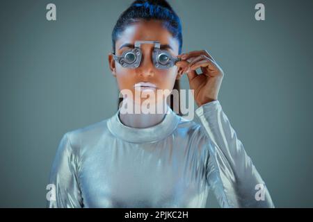 Model dressed as a silver robot Holding prosthesis looking at camera on grey background Stock Photo