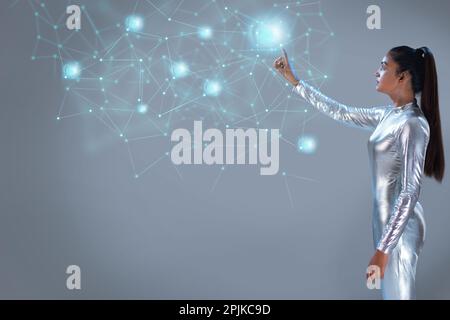 A woman wearing silver futuristic clothes touching a virtual icons on a virtual Screen Stock Photo