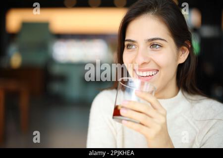 Happy woman drinking soda in a restaurant looking away in a restaurant Stock Photo