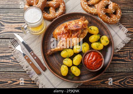 Oktoberfest festival food half fried chicken with boiled potatoes, sauce, beer and pretzels close-up on a wooden table. Horizontal top view from above Stock Photo