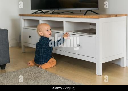 Toddler baby boy open cabinet drawer with his hand. Child explore what is in cabinet. Baby curiosity and child development stages Stock Photo