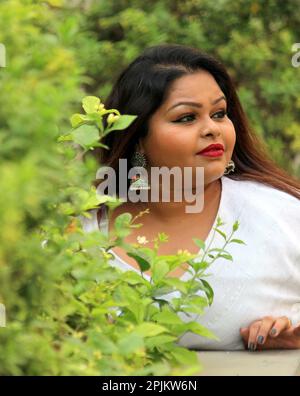 A plus size model posing with a side face looking at her left side wearing white cloths and a beautiful earing Stock Photo