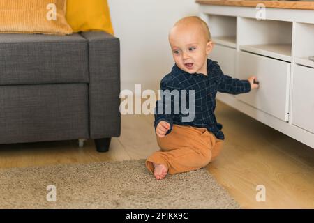 Toddler baby boy open cabinet drawer with his hand. Child explore what is in cabinet. Baby curiosity and child development stages concept Stock Photo