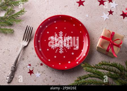Red plate with white polka dots and snowflake with a gift in craft paper tied with a red ribbon decorated with a Christmas spruce branches and confett Stock Photo