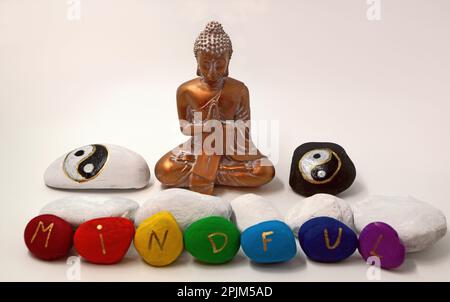 Gold colored Buddha figure with hand-painted stones. Two stones with Yin-Yang signs in black and white. The others have the word mindful written on th Stock Photo