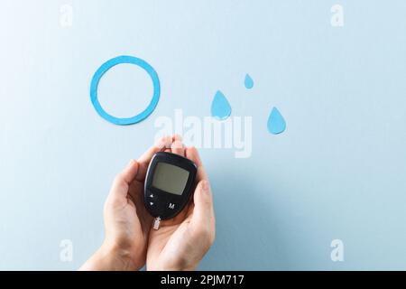 Hands of caucasian woman holding glucometer over blue drops and ring on blue background Stock Photo