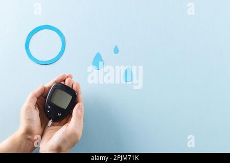 Hands of caucasian woman holding glucometer over blue drops and ring on blue background, copy space Stock Photo