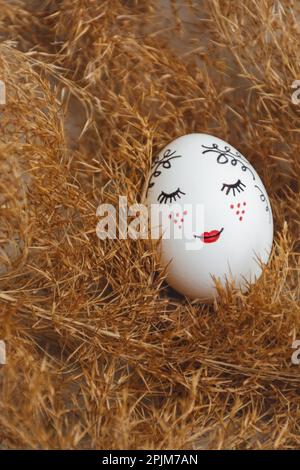 Easter greeting card. Hand-painted Easter egg lie in dry natural pampas grass. Painted gentle face. Dry golden reed. Soft selective focus Minimalistic style. Copy Space Stock Photo