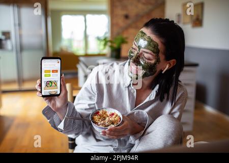 Close up of a Young adult woman showing off a dieting app to someone over a video call Stock Photo