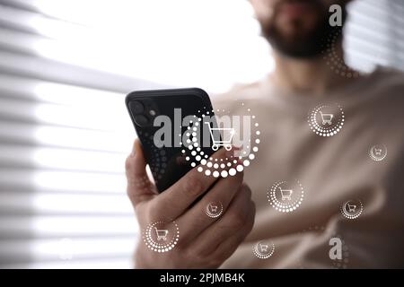 Delivery concept. Man using modern mobile phone for online shopping indoors, closeup. Market cart illustrations Stock Photo