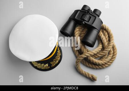 Peaked cap, rope and binoculars on light grey background, flat lay Stock Photo