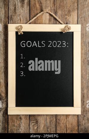 Blackboard with phrase GOALS 2023 and empty checklist on hanging on wooden background Stock Photo