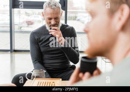 bearded middle aged man smelling puer tea near bearded friend on blurred foreground,stock image Stock Photo