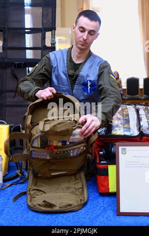 Man Ukrainian army medic presenting backpack with soldier first aid kit: bandages, wound-healing drugs, balloon with burn-treating gel, painkillers. O Stock Photo