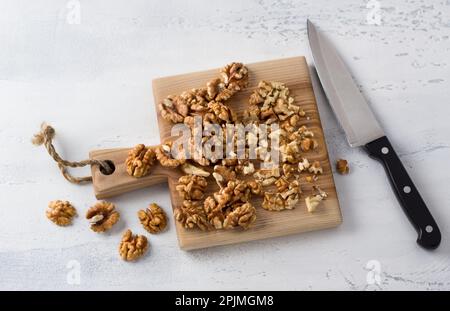 Wooden board of chopped walnuts with a knife on a light gray textured background, home cooking, top view Stock Photo